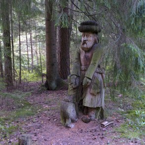 Wooden sculpture in the forest with a seated figure and an animal carving Wooden sculpture in the forest with a seated figure and an animal carving
