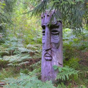 Wooden face sculpture among ferns in a dense forest setting Wooden face sculpture among ferns in a dense forest setting