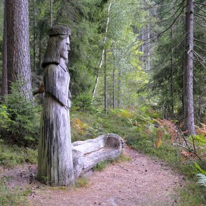 Wooden female sculpture in the forest by a trail with a log bench Wooden female sculpture in the forest by a trail with a log bench