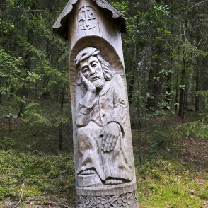 Wooden relief sculpture of a man under a small roof by a forest trail Wooden relief sculpture of a man under a small roof by a forest trail