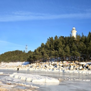 Winter landscape at Užava beach with lighthouse and walkers on ice Winter landscape at Užava beach with lighthouse and walkers on ice