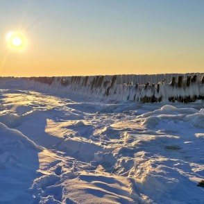Ziemas saules mirdzums virs apledojušiem koka steķiem Papē Ziemas saules mirdzums virs apledojušiem koka steķiem Papē