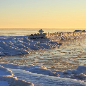 Apledojuši Papes koka steķi un sasalusi jūra saulrietā Apledojuši Papes koka steķi un sasalusi jūra saulrietā