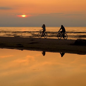 Riteņbraucēji saulrietā pludmalē Riteņbraucēji saulrietā pludmalē