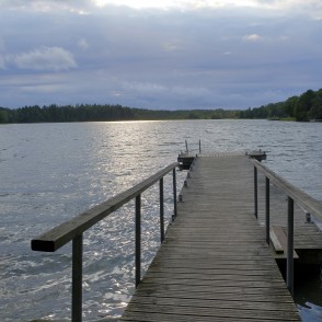 Koka laipa Plateļu ezerā ar saules atspīdumu uz ūdens zem mākoņainām debesīm Koka laipa Plateļu ezerā ar saules atspīdumu uz ūdens zem mākoņainām debesīm
