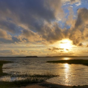 Saulriets virs ezera ar zeltainu atspīdumu un dramatiskām mākoņu formām Saulriets virs ezera ar zeltainu atspīdumu un dramatiskām mākoņu formām