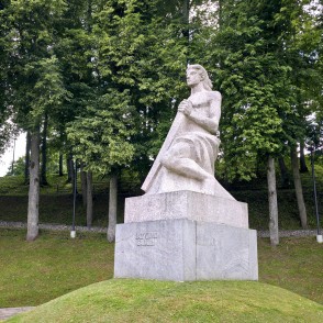 Piemineklis Koklētājs Talsos uz zaļojoša koku fona Piemineklis Koklētājs Talsos uz zaļojoša koku fona