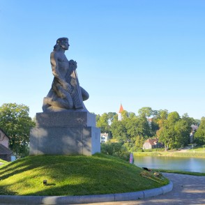 Piemineklis Koklētājs Talsos uz pilsētas un ezera fona Piemineklis Koklētājs Talsos uz pilsētas un ezera fona