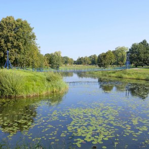 Pedestrian bridge over the Bārta River with aquatic plants and park landscape Pedestrian bridge over the Bārta River with aquatic plants and park landscape
