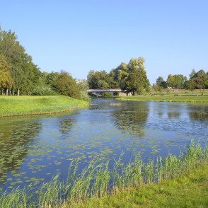 Bārta River with a bridge and well-kept park landscape in the background Bārta River with a bridge and well-kept park landscape in the background