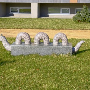 Akmens skulptūra čūskas tēlā uz zāliena pie celiņa Akmens skulptūra čūskas tēlā uz zāliena pie celiņa