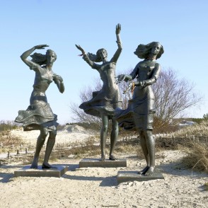Skulptūra "Zvejnieka meitas" smilšu kāpās ar zilām debesīm Skulptūra "Zvejnieka meitas" smilšu kāpās ar zilām debesīm