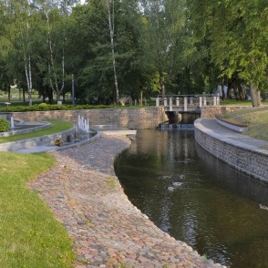 Gleznains kanāla līkums ar tiltiņu un strūklakām Marijampoles dzejas parkā Gleznains kanāla līkums ar tiltiņu un strūklakām Marijampoles dzejas parkā
