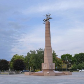 Piemineklis Tautai un valodai Marijampoles laukumā uz koku fona Piemineklis Tautai un valodai Marijampoles laukumā uz koku fona